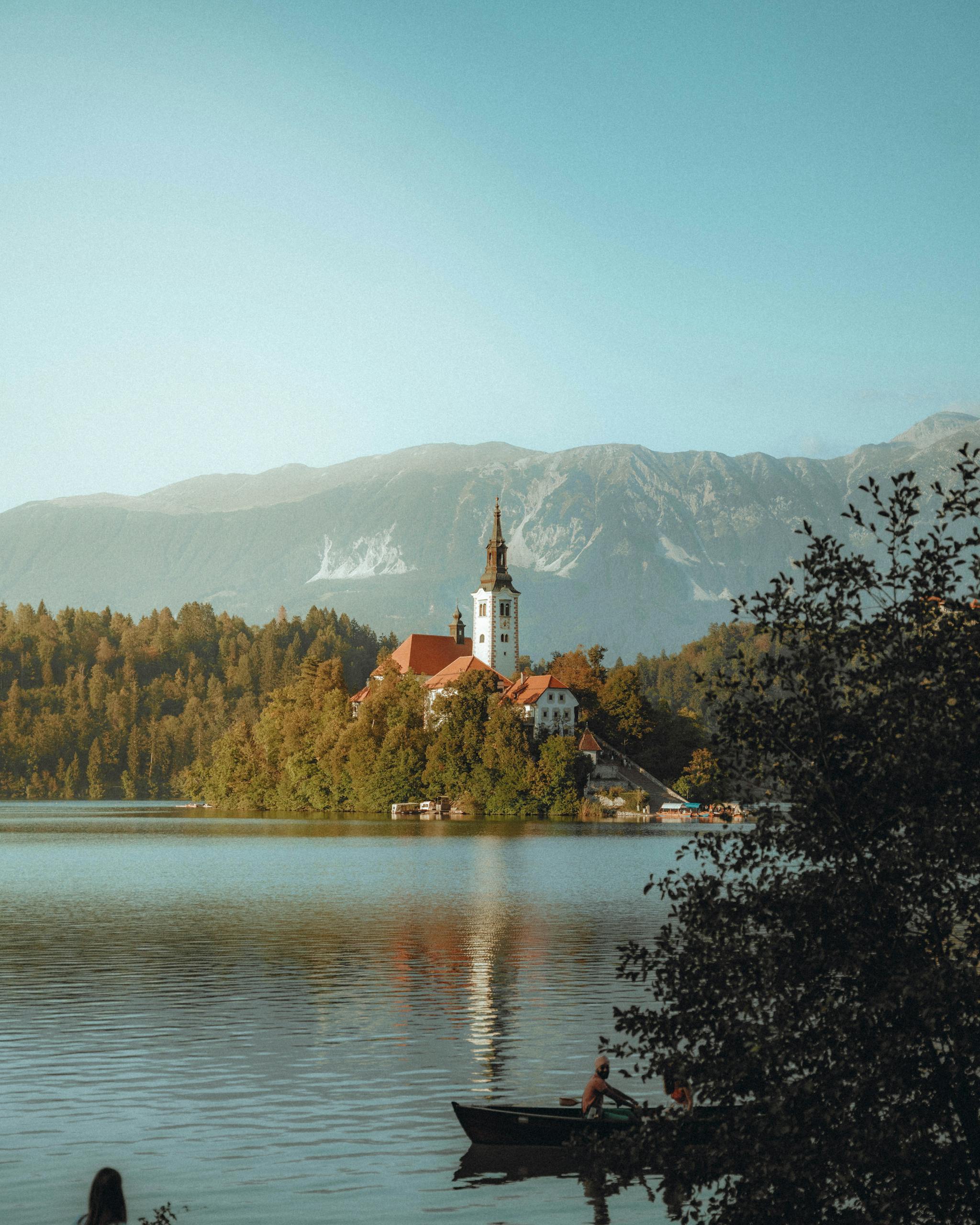 Bled Island with the Church of the Assumption, surrounded by Lake Bled and scenic mountains at sunset.