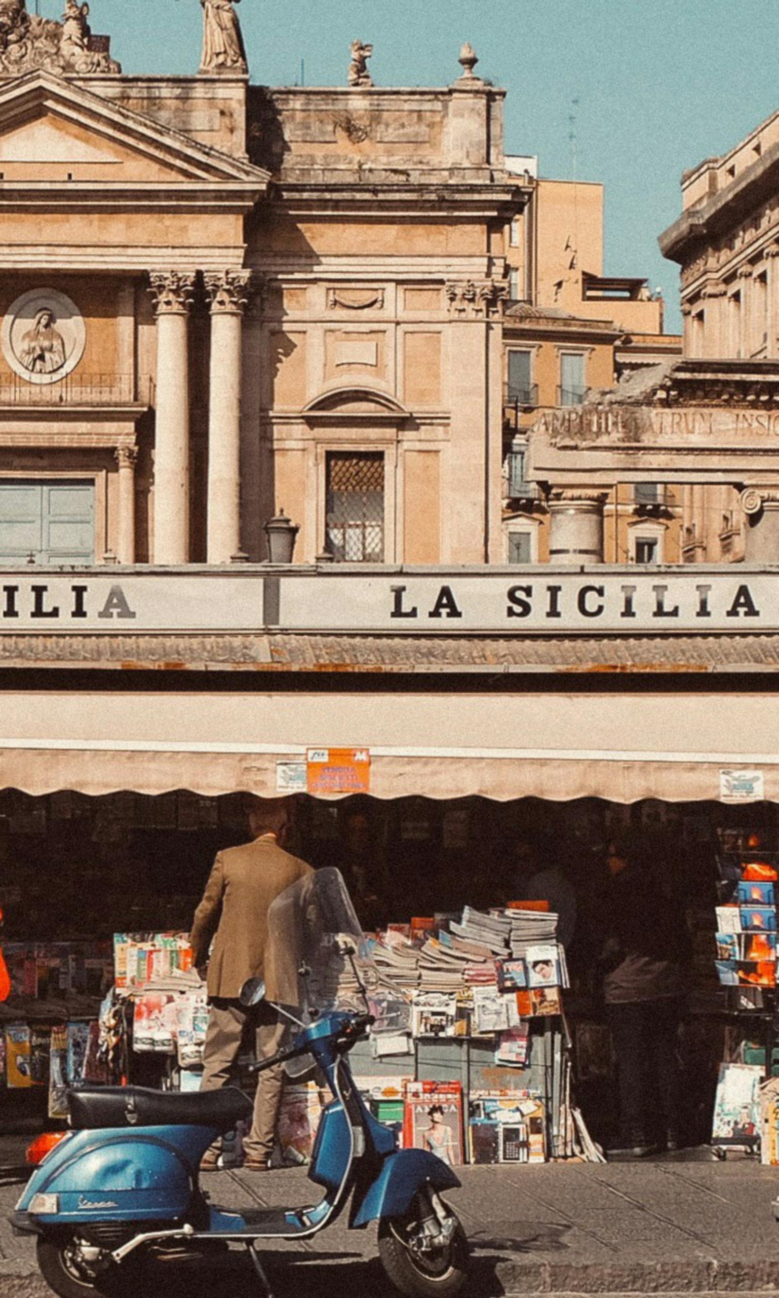 Charming Sicilian street scene with a kiosk, scooter, and historic architecture.