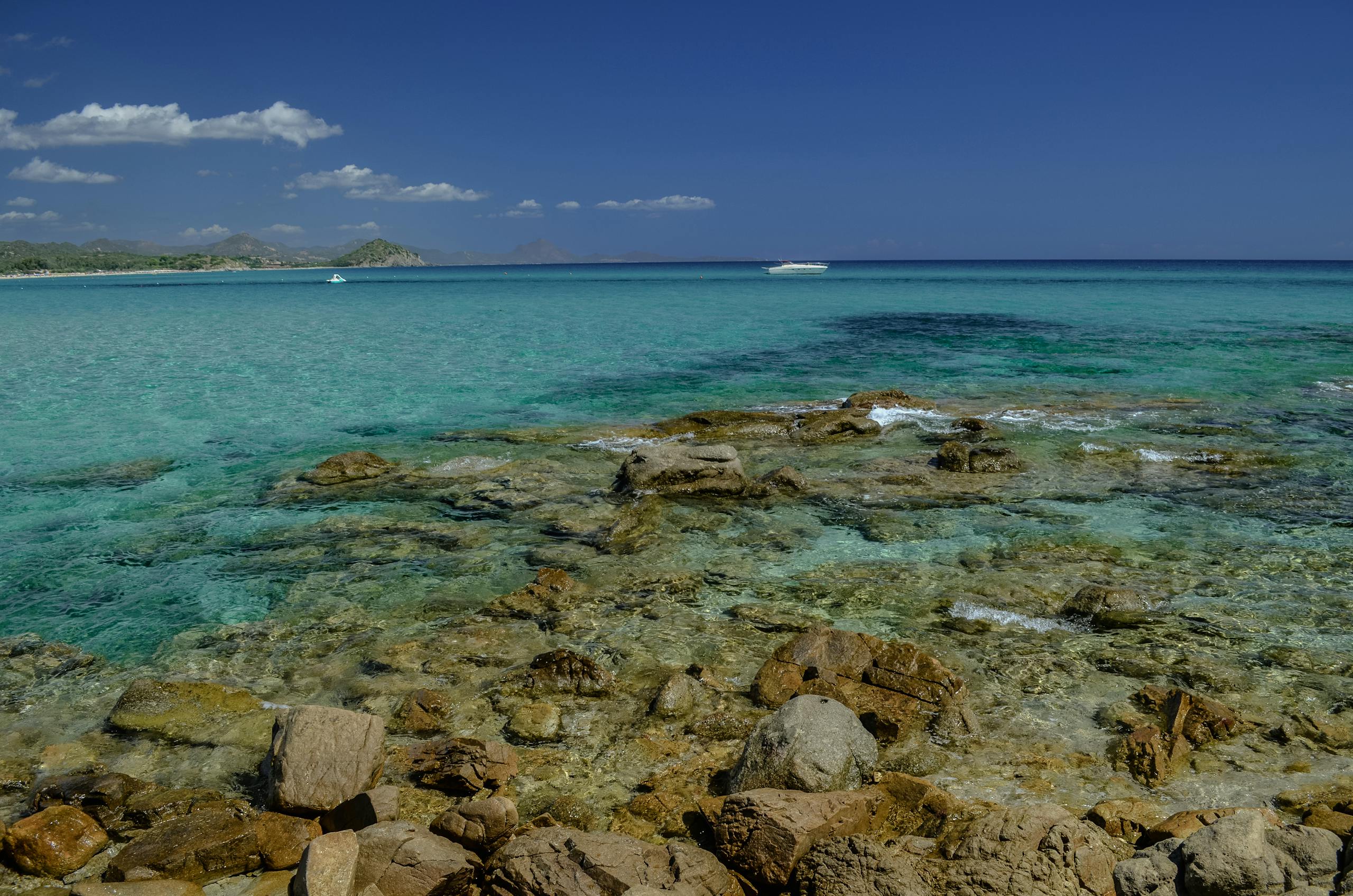 Stunning clear turquoise waters and rocky shores of a Sardinian beach under a bright blue sky.