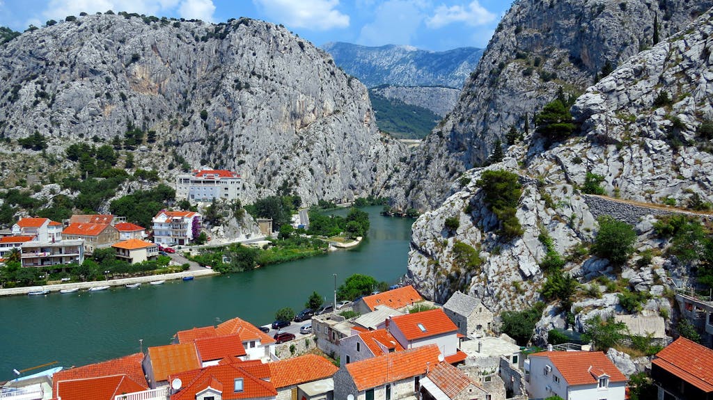 Stunning landscape of Omis, Croatia with a river winding through rugged mountains and red-roofed houses.